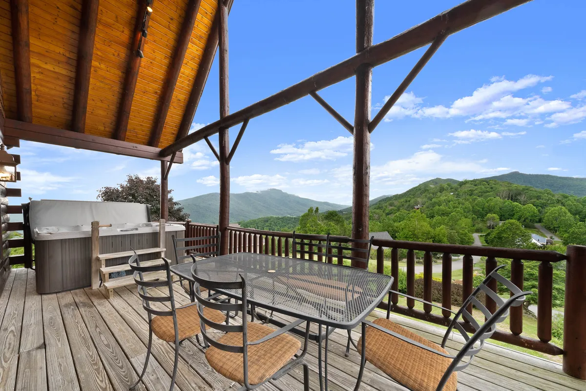 A wide shot showcasing the upper deck's main amenities: an outdoor dining table set for al fresco meals, a hot tub, and sweeping mountain views. The golden light hints at sunset, amplifying the atmosphere of tranquil evenings and social gatherings.
