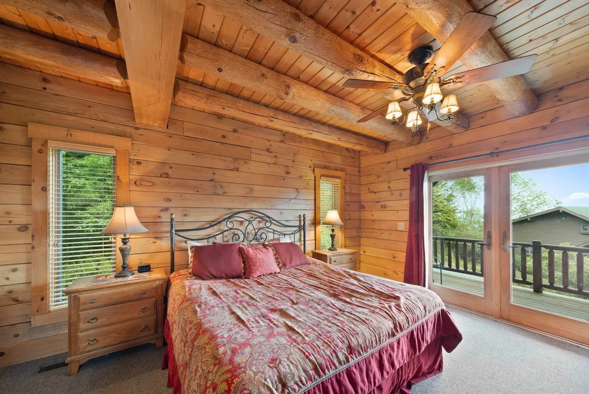 A spacious bedroom featuring a plush King bed with decorative bedding, exposed wooden ceiling beams, and large sliding glass doors that open to a private deck. The room exudes warmth and comfort, with ample natural light and a sense of privacy.