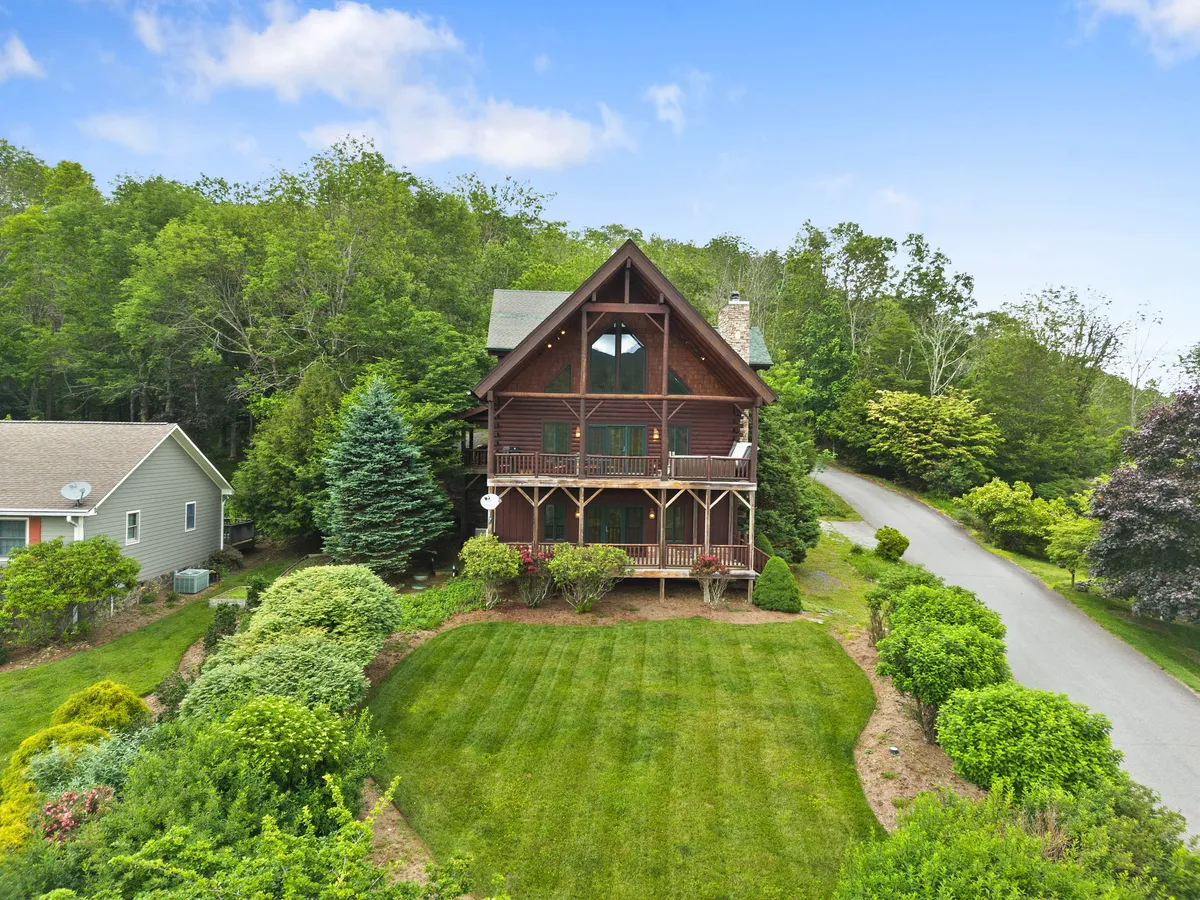 A picturesque A-frame cabin is surrounded by lush greenery and a well-manicured lawn. The balconies and expansive outdoor space suggest opportunities for outdoor gatherings, sunsets on the balcony, and easy access to nearby nature trails.