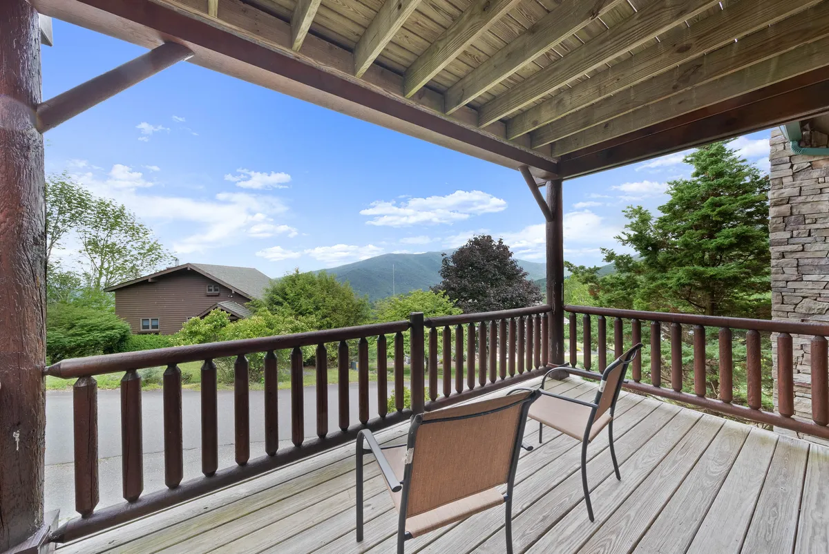 A tranquil outdoor deck with wooden railings and comfortable chairs overlooks sweeping mountain vistas. The scene radiates serenity, capturing both the spaciousness of the deck and the natural beauty of the Blue Ridge Mountains. The setup is ideal for relaxing with a morning coffee or stargazing at night, and alludes to the hot tub experience described in the section.