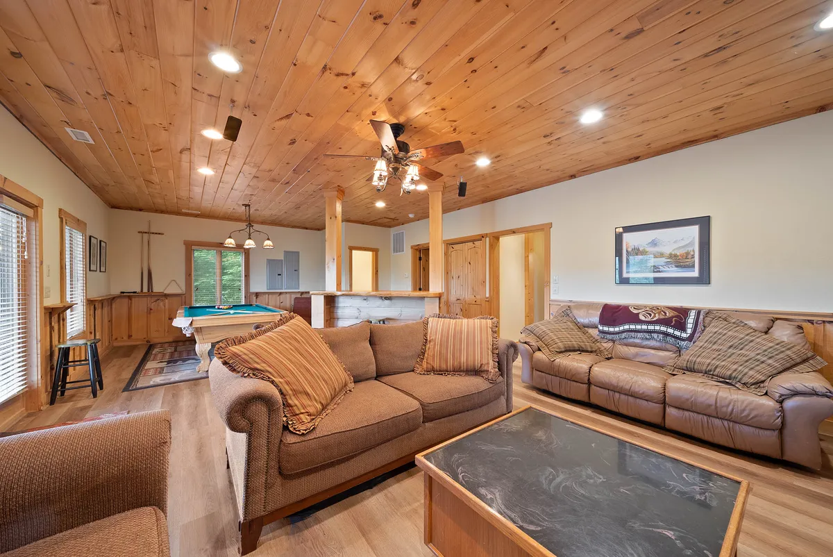 This image showcases a spacious entertainment room with comfortable sofas, a coffee table, a pool table, and large windows letting in natural light. The setup invites relaxation as well as social interaction, hinting at both movie nights and game sessions.