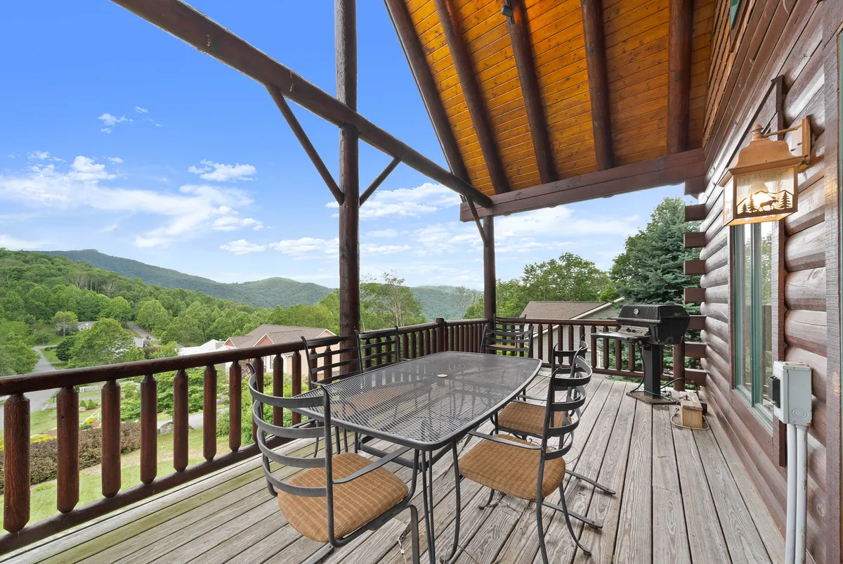 A close view of the outdoor dining table, positioned on the deck with a gas grill nearby and panoramic mountain scenery in the background. The scene suggests a space ideal for grilling and sharing stories with friends and family.