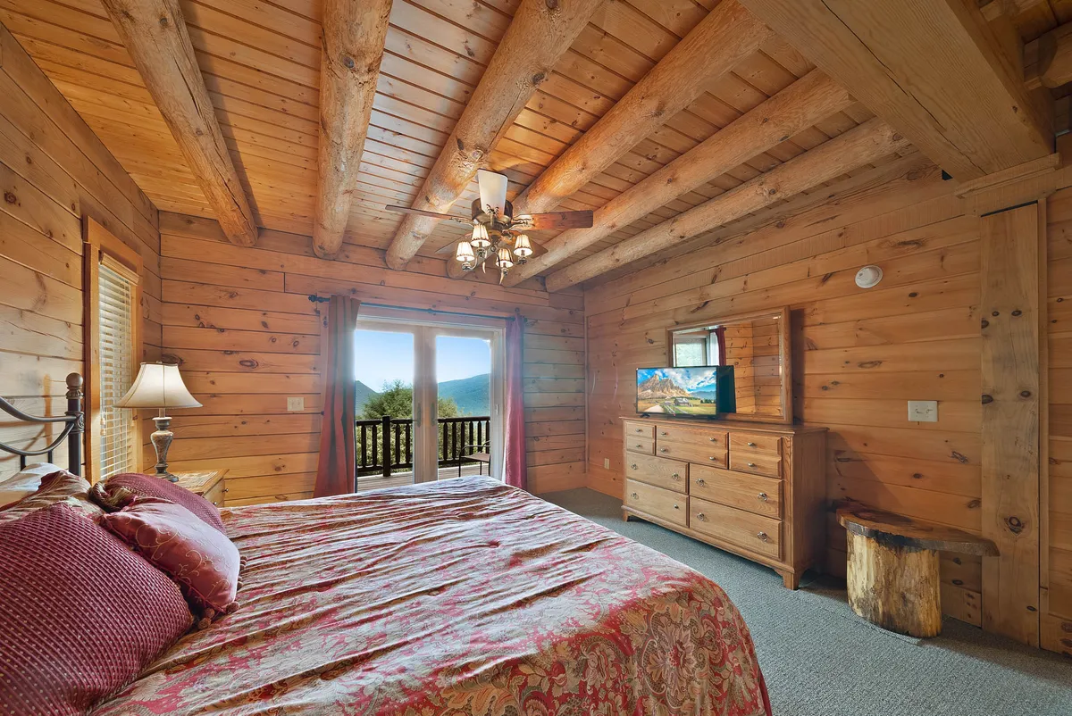 A serene bedroom with a King bed featuring ornate bedding, large windows offering scenic views, and classic wooden furniture. The room balances comfort, elegance, and a connection to the outdoors, ideal for restful nights or peaceful mornings.