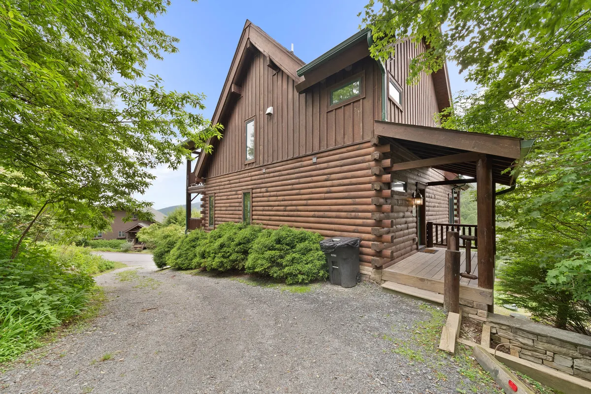 A cozy log cabin-style exterior with lush green shrubs and a stone pathway leading to the entrance. The inviting porch and natural landscaping highlight the property’s connection to the outdoors.