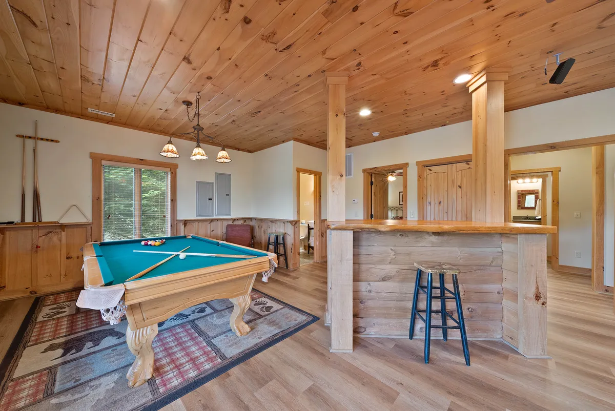 An inviting interior with a pool table, bar area, and large windows that frame the outdoor scenery. The space is set up for social gatherings, game nights, and relaxing with friends after an active day.